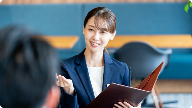 資料を手に笑顔で説明をするスーツ姿の女性ビジネスパーソン